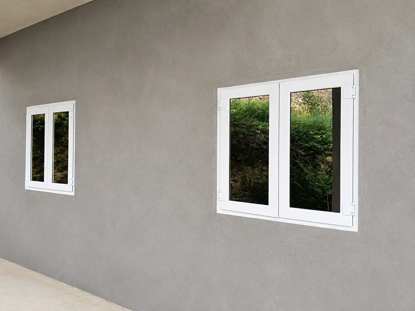 Dos ventanas blancas instaladas sobre una pared exterior gris
